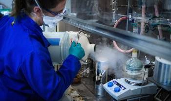 woman pours steaming vessel into smaller container under fume hood